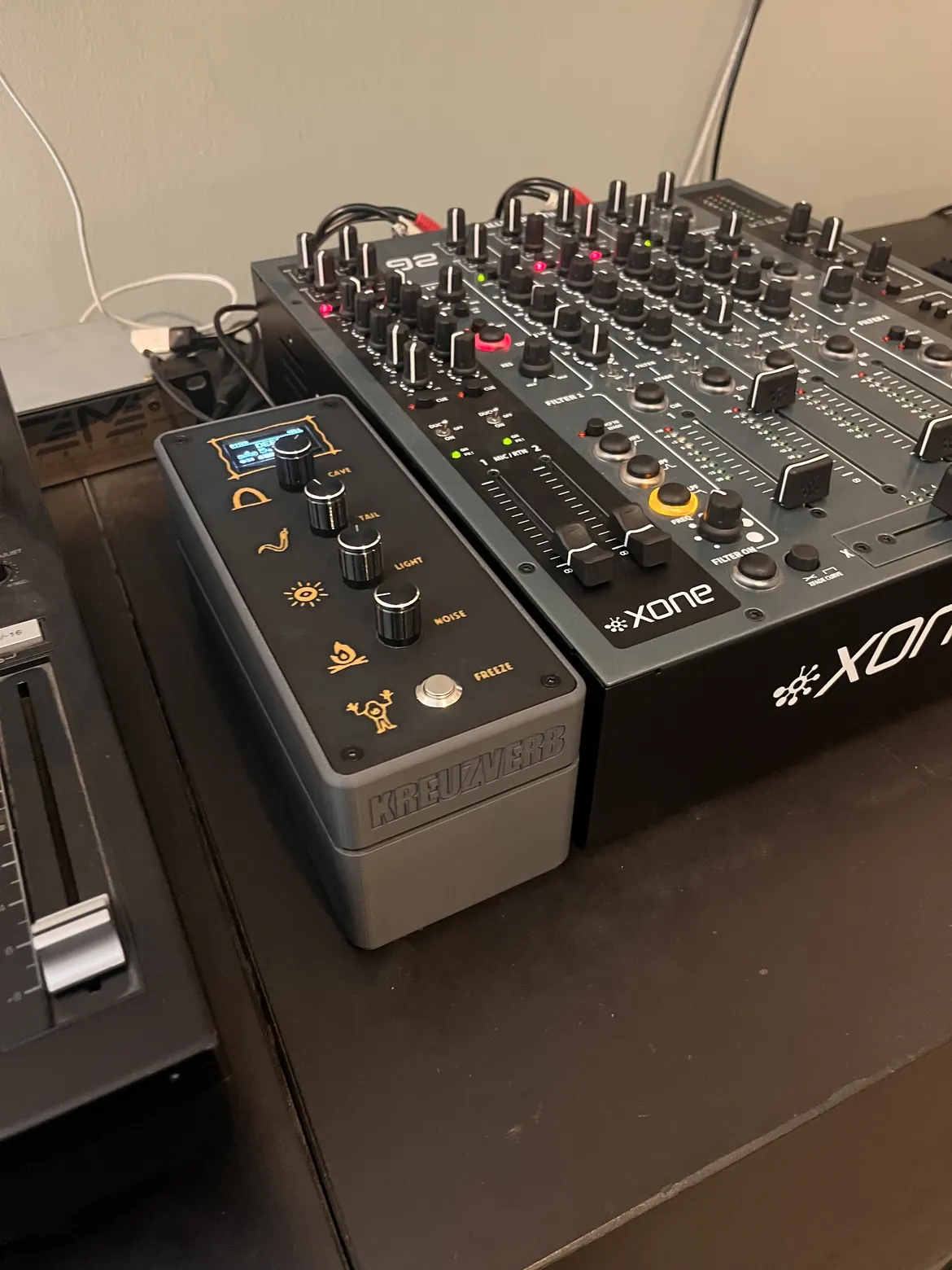 The first KREUZVERB, dark gray case with a black panel, four knobs and orange cave signs, standing flush next to a Xone:92 on a desk.